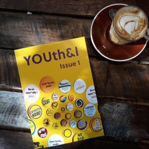 Single copy of Issue 1 in print on a wooden table with a cup of coffee next to it. 