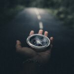 Hand outstretched holding a compass to guide the way. Background is a blurred road.