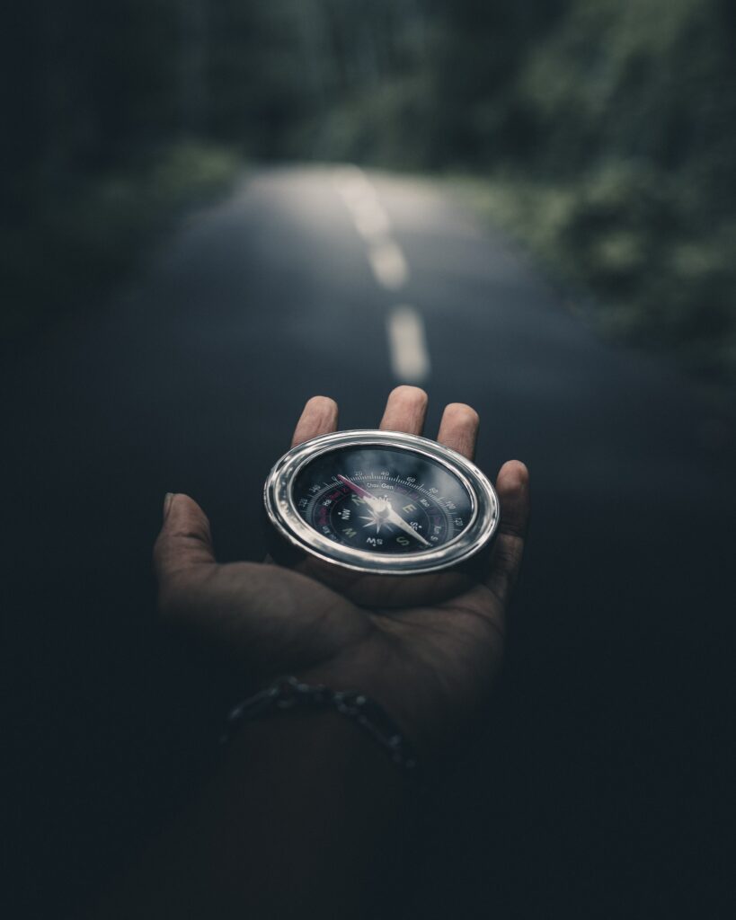 Hand outstretched holding a compass to guide the way. Background is a blurred road.