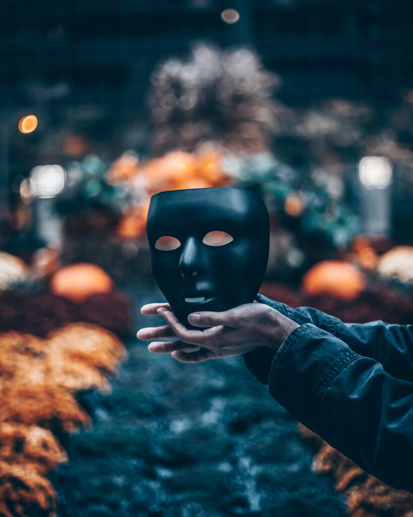 Hands holding a black mask. In the background are blurred colours.