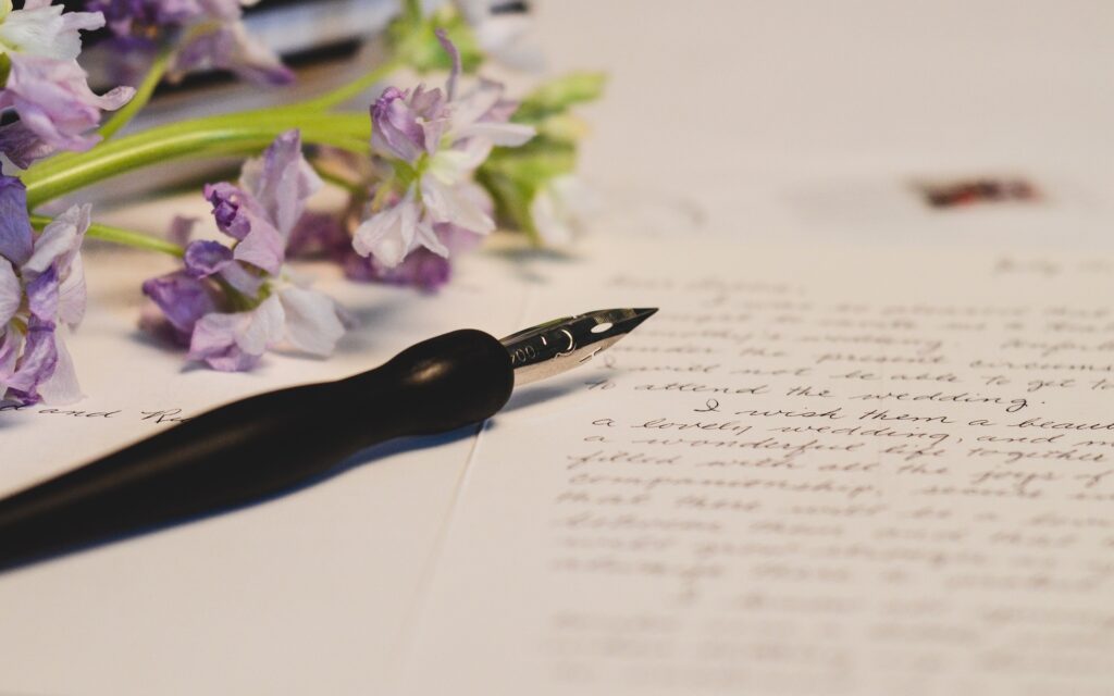 Image of a fountain pen and a letter with cursive writing. There are pink flowers next to the page.