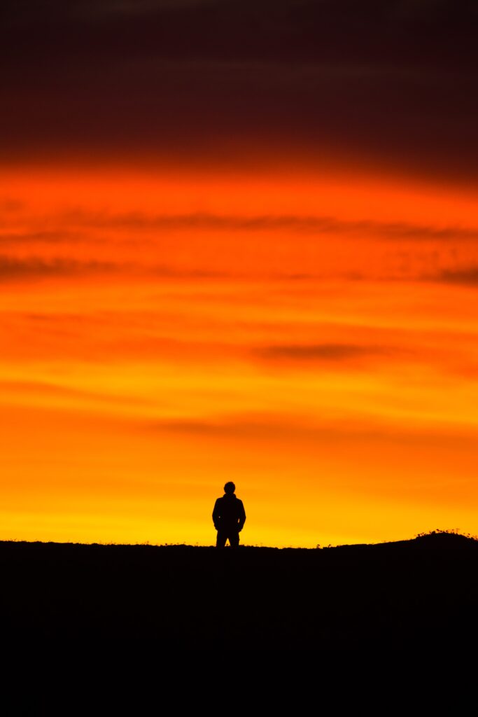 Silhouette of man standing in front of bright orange sunset